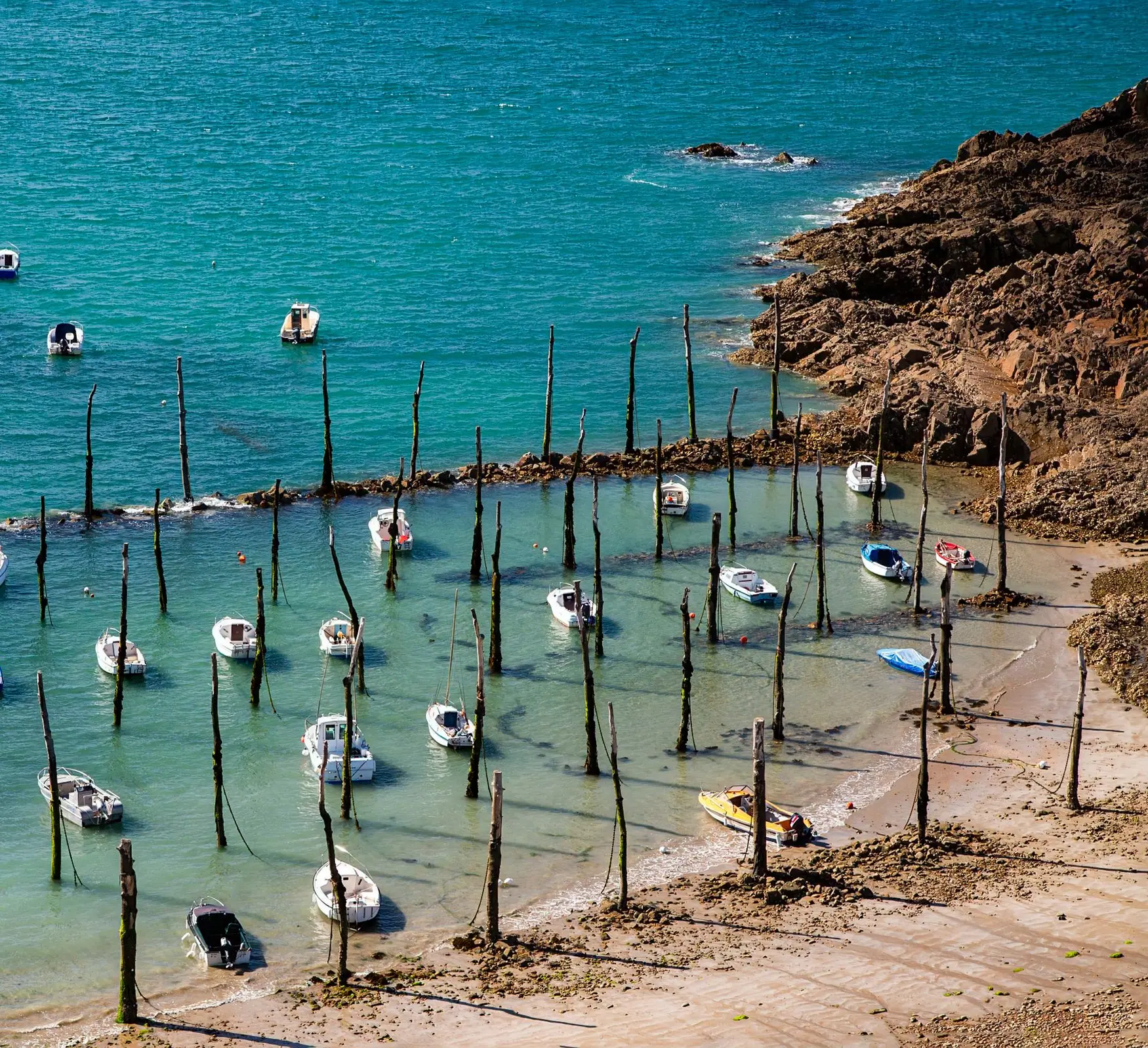 Petits bateaux sur leurs mouillages entre des pieux, eau turquoise à marée basse