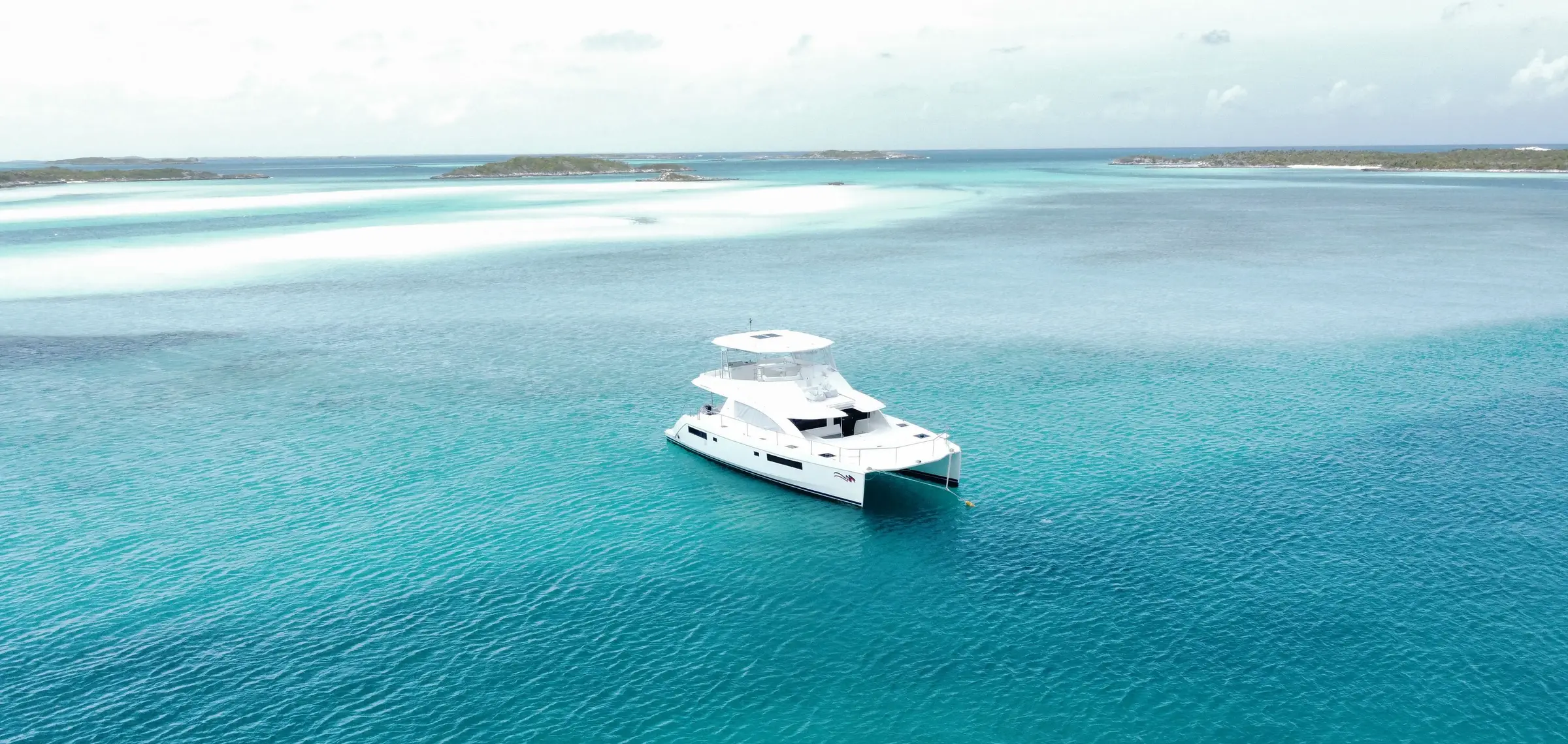 Capon, catamaran à moteur blanc, au mouillage sur une eau turquoise peu profonde