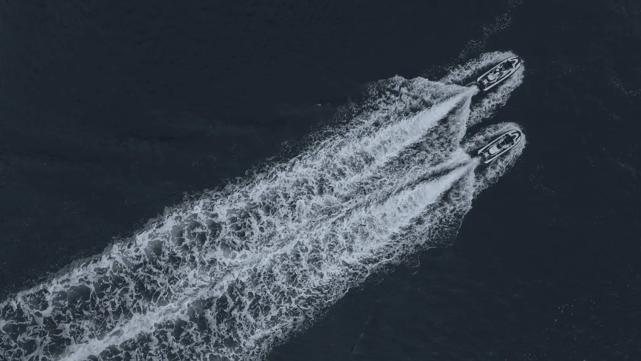 Deux jets-skis vus du ciel, côte à côte, leurs sillages sur une eau sombre