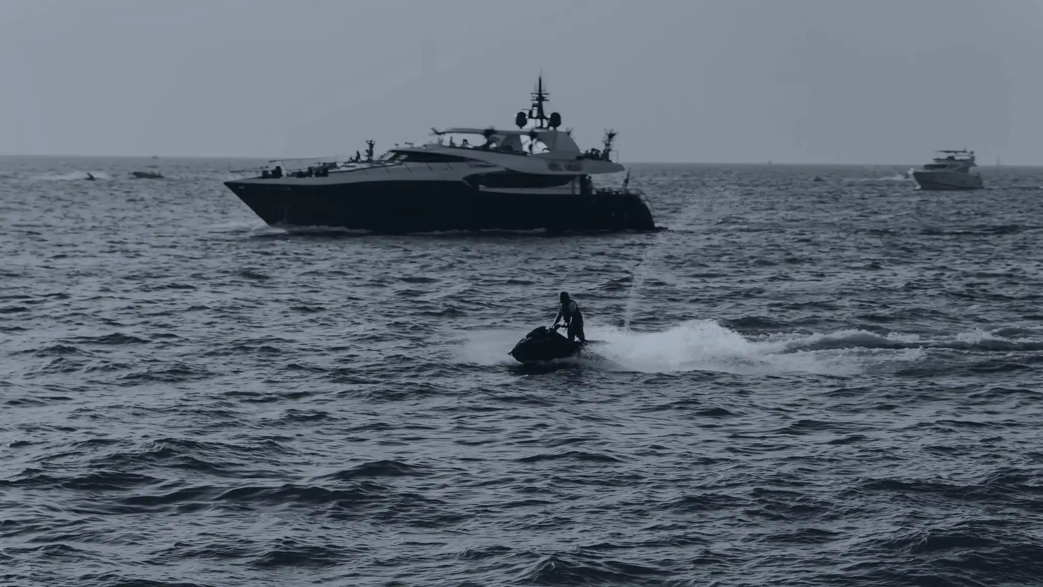 Un pilote debout sur son jet-ski, un yacht au large