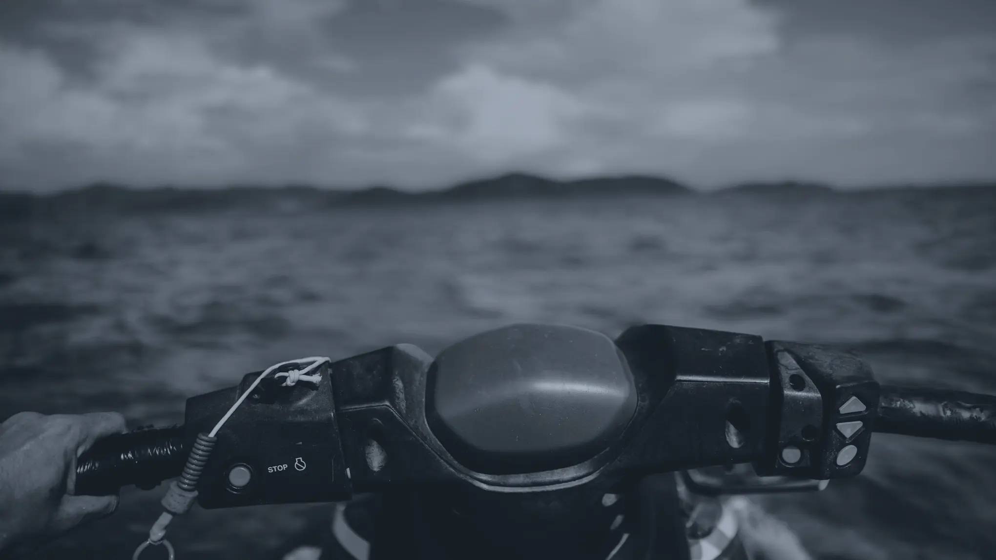Le guidon vu depuis la selle : la main sur la poignée, le cordon du coupe-circuit, la mer devant
