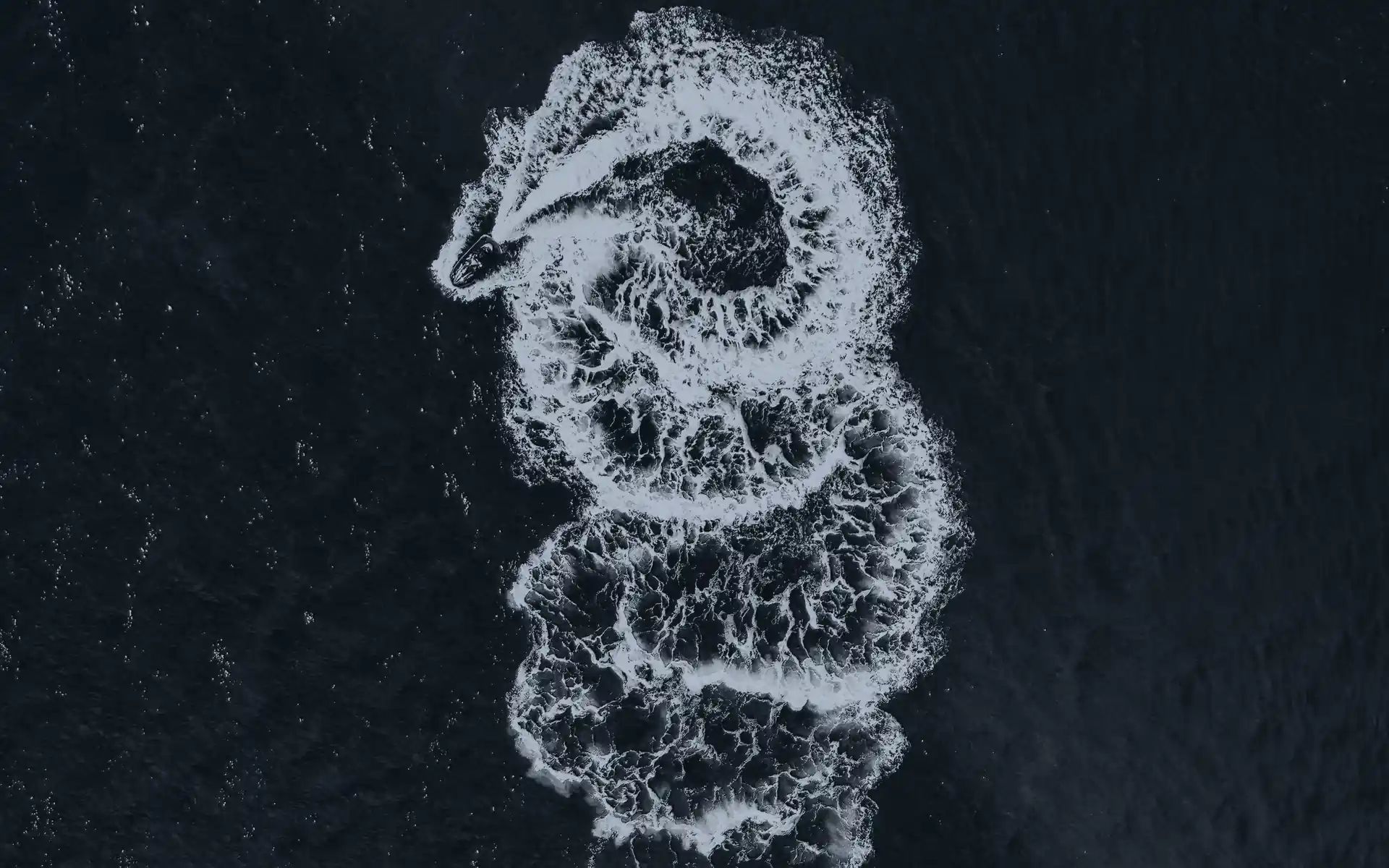Vu du ciel, le sillage en boucles d’un jet-ski sur une eau sombre