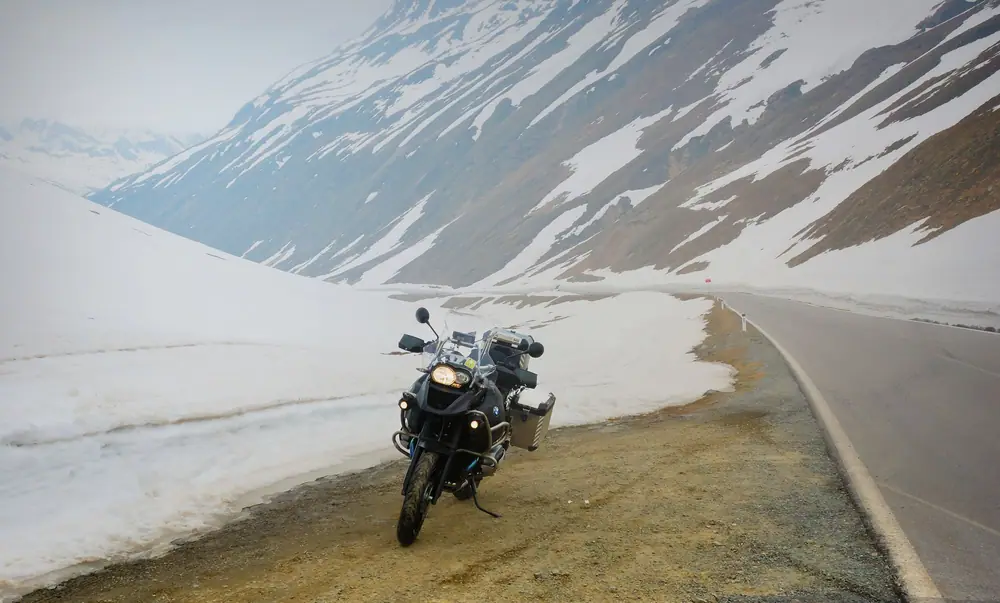 Gros trail à valises garé entre deux murs de neige, au bord d’une route de col
