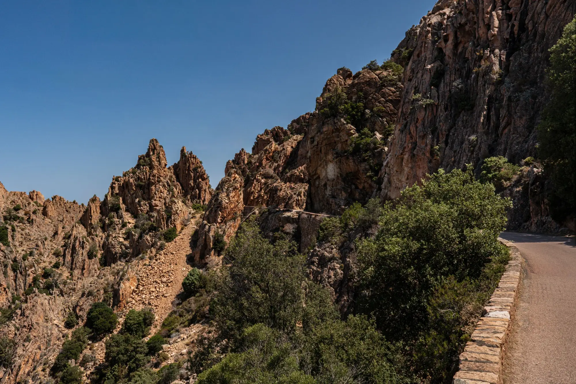 La D81 longe les aiguilles de granite rouge, derrière un parapet de pierre.