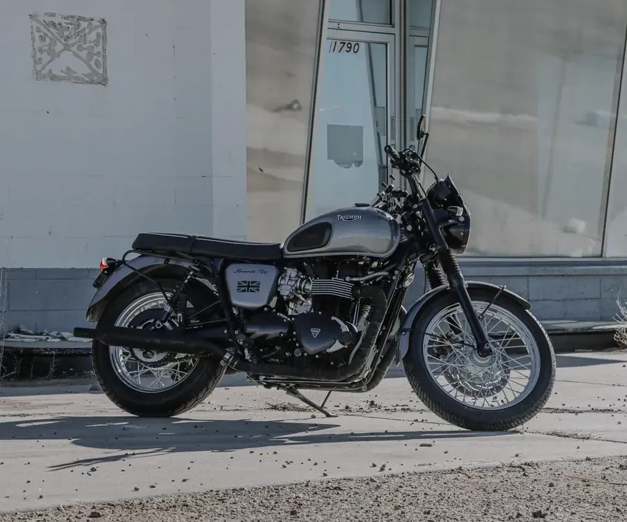 Triumph Bonneville T100 grise de profil, roues à rayons, devant une vitrine