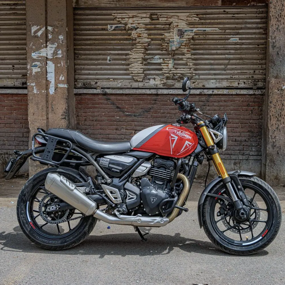 Triumph Scrambler 400 X rouge et noire de profil, fourche dorée, devant un rideau de fer