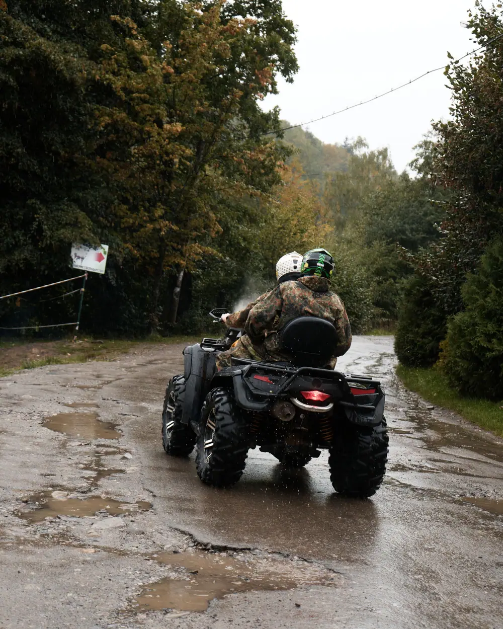 Quad biplace vu de dos sur une route mouillée, pilote et passager casqués