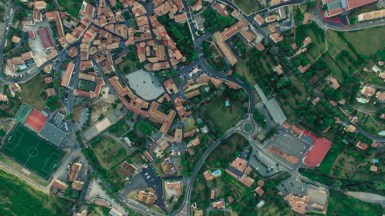 Vue aérienne verticale du bourg des Vans : toits de tuiles, rues, stade