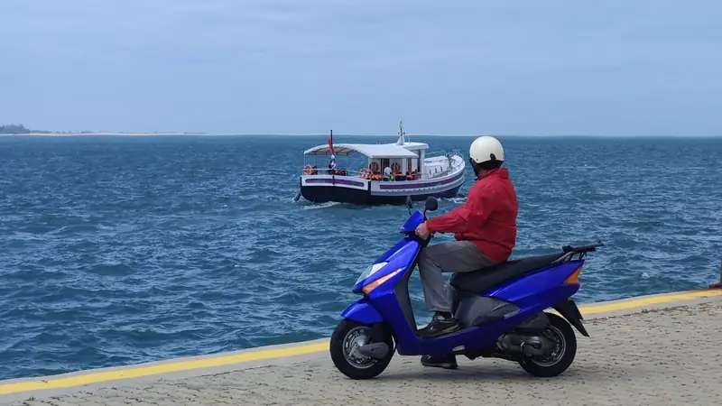 Un scooter bleu arrêté sur le quai, face au bateau qui arrive