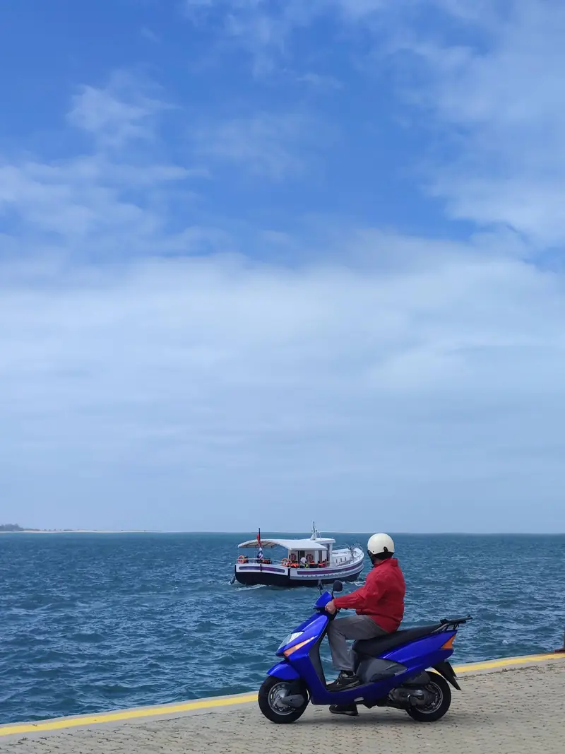 Un scooter bleu arrêté sur le quai, face au bateau qui arrive