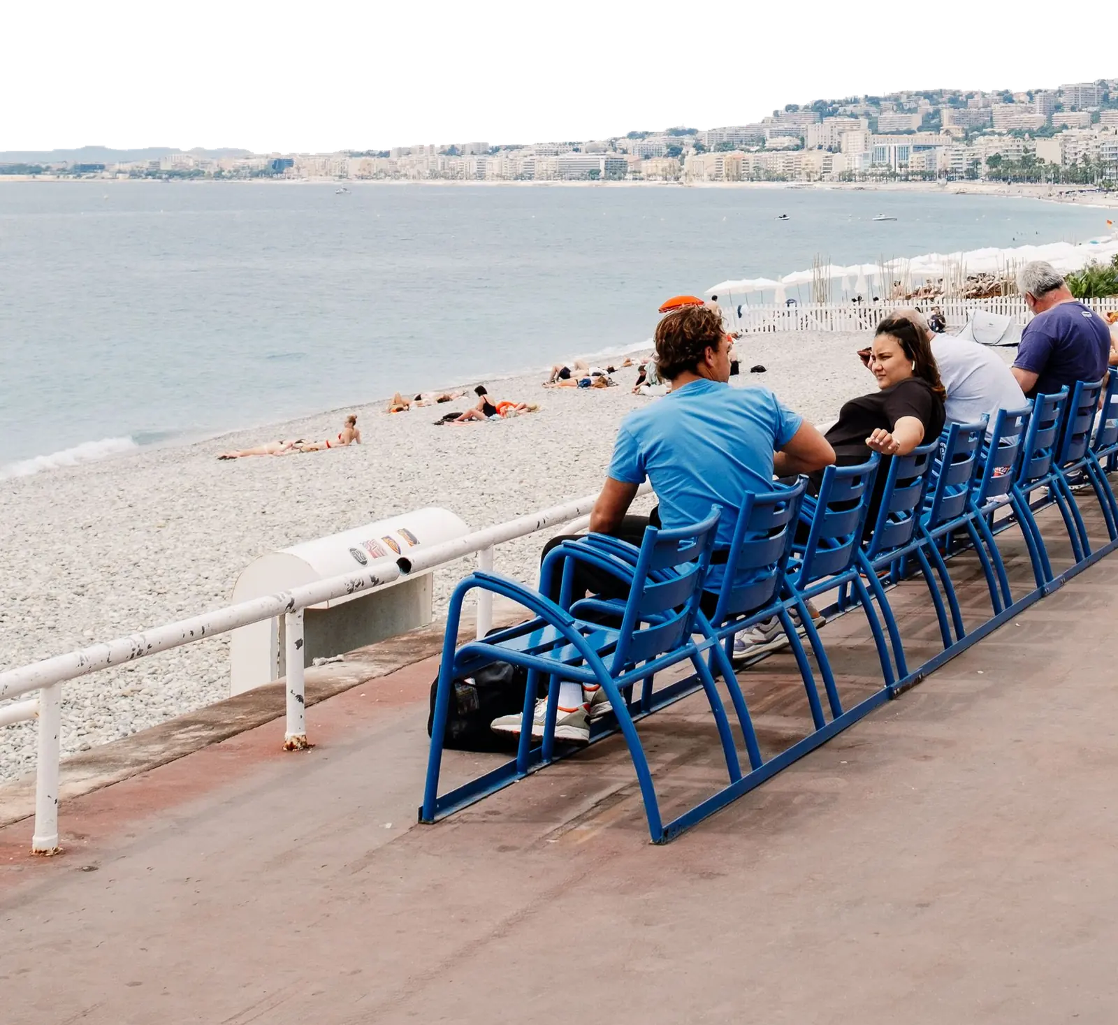 Promenade des Anglais : une rangée de chaises bleues face à la baie des Anges, des promeneurs assis de dos