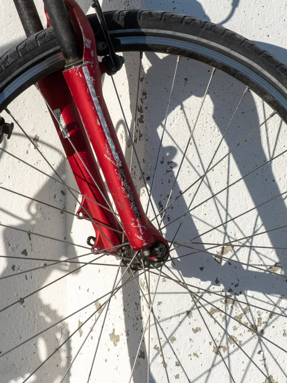 Roue et fourche rouges d’un vélo, contre un mur blanc.