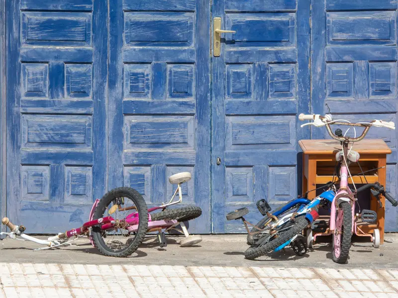 Trois vélos d’enfants posés devant une porte bleue.