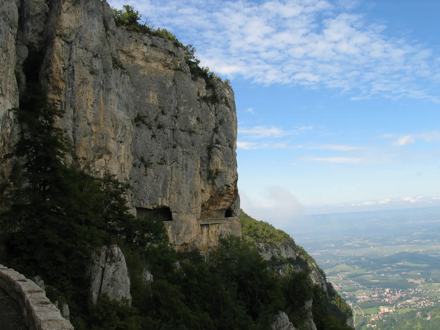 La route en corniche sous une falaise de calcaire, deux tunnels, la plaine en contrebas
