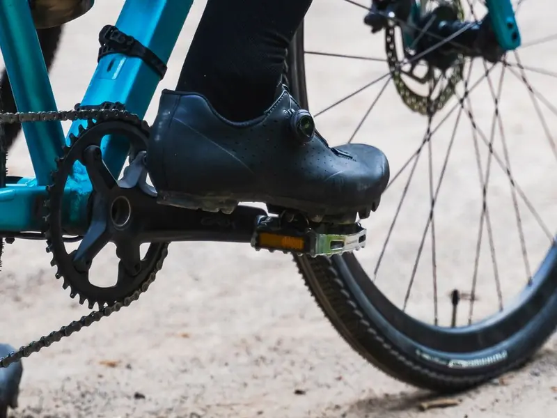 Chaussure de gravel à semelle crantée sur la pédale d’un gravel bleu, côté pédalier