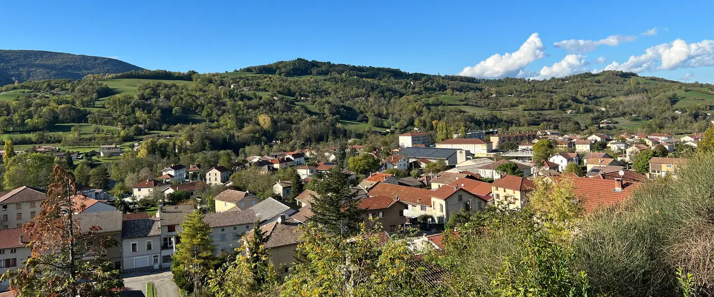 Les toits de tuiles de Saint-Jean-en-Royans et les collines boisées, en automne, sous un ciel bleu